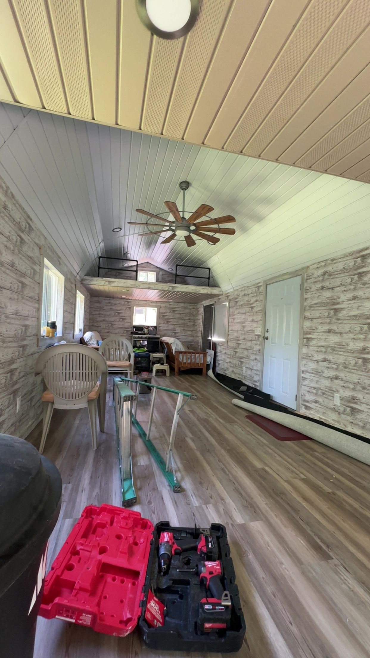 Interior renovation: room with wood ceiling and walls. Tools on floor, furniture in the background.