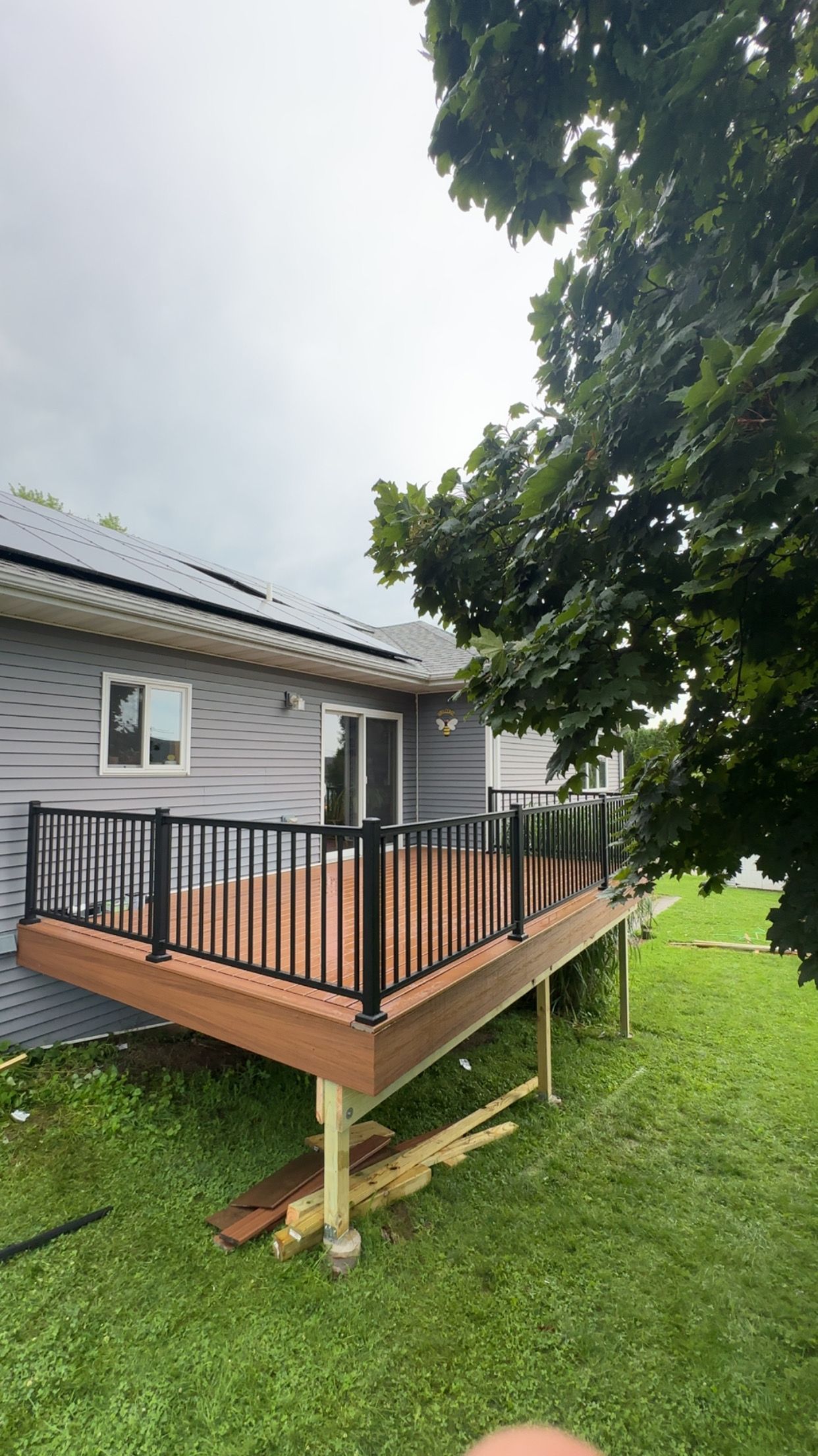 Wooden deck with black railing, gray siding, and green grass under a cloudy sky.