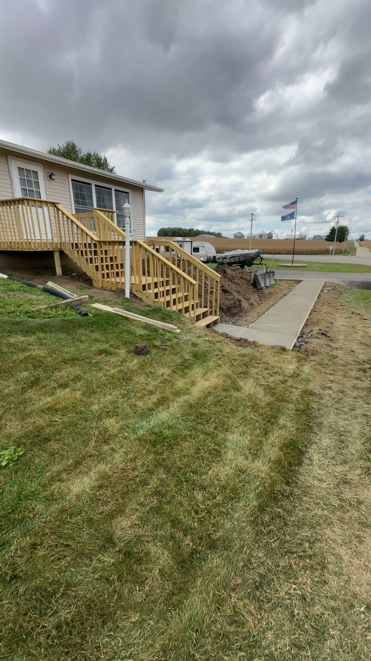 Exterior of a building with wooden stairs, sidewalk, and grassy hill on a cloudy day.