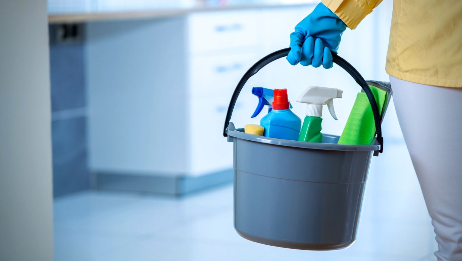 Woman in gloves sprays and wipes a desk in a classroom, preparing it for students.