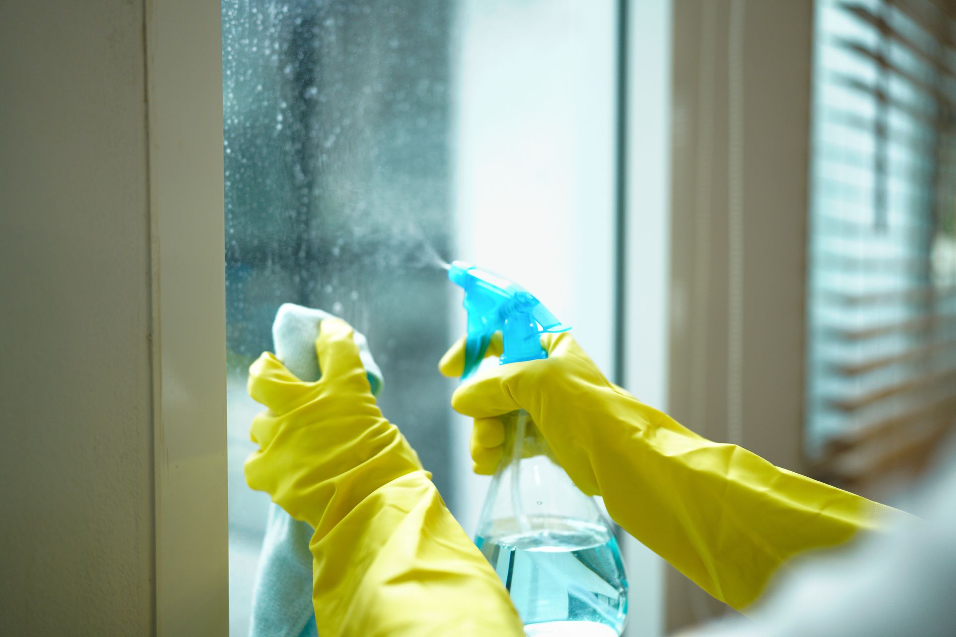 Man cleaning a milking parlor with a hose; blue and gray equipment, boots, industrial setting.