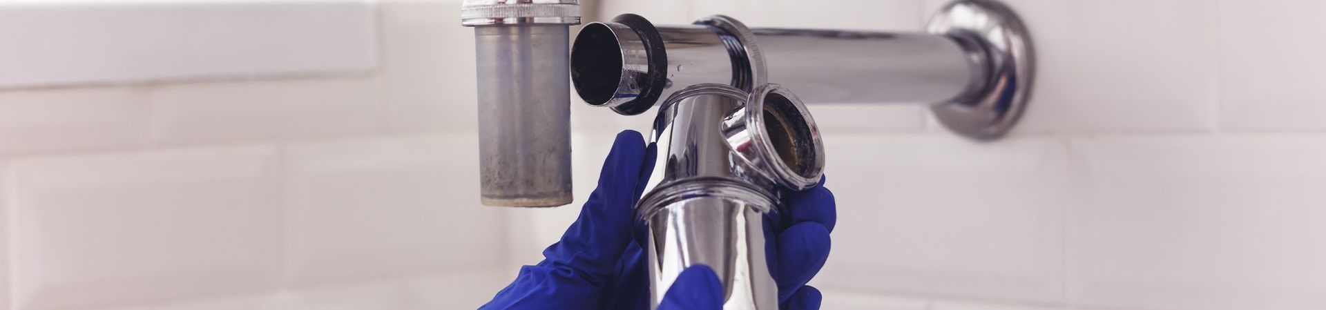 A person wearing blue gloves is fixing a sink drain.