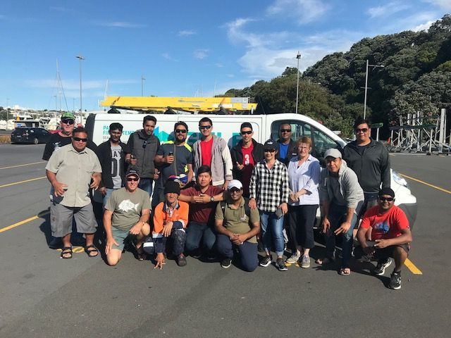 Group of people posing by a van in a parking lot on a sunny day.