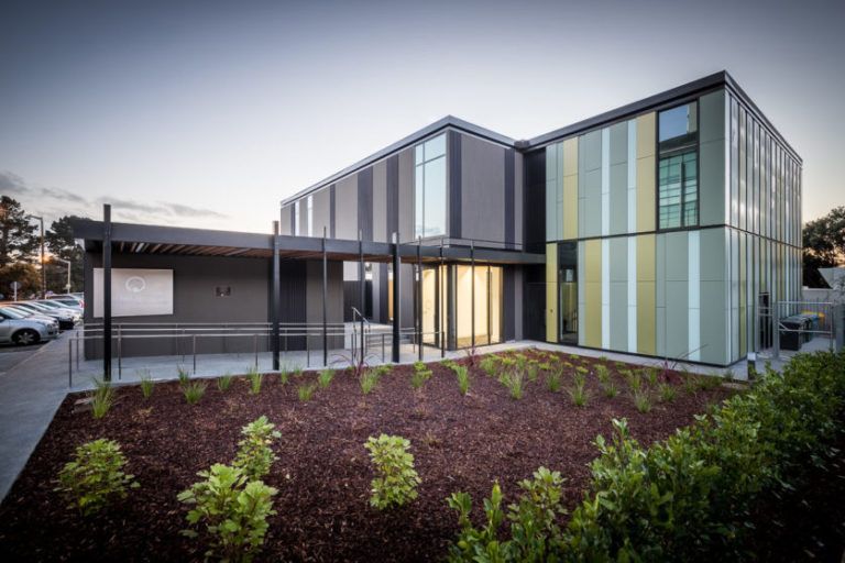 Modern building with multi-colored panel siding, a covered entrance, and landscaped garden.