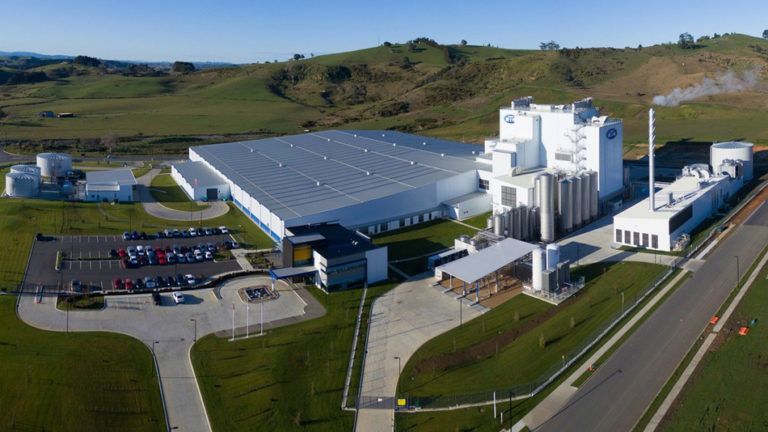 Large industrial dairy processing plant with silos, a long building, and parking lot on a green landscape.