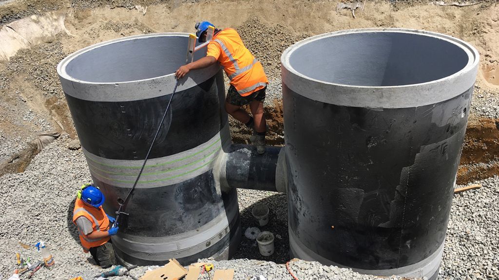 Construction workers connecting large concrete drainage pipes at a construction site.
