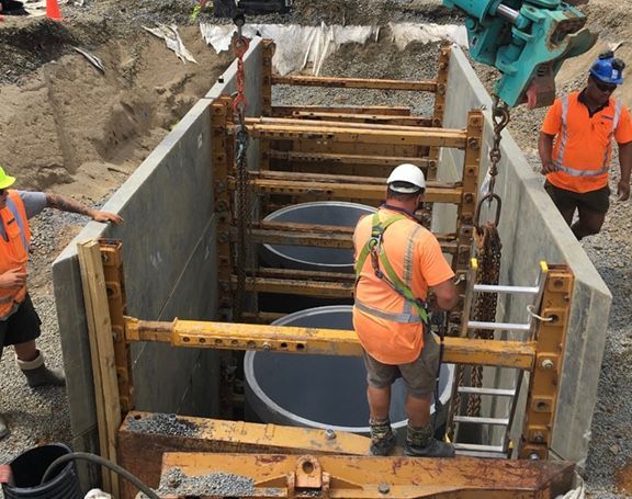 Construction workers installing circular tanks in a trench, using safety equipment.