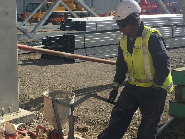 Construction worker in a safety vest and hard hat pours material at a construction site.