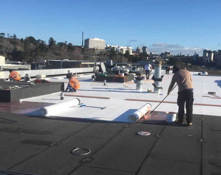 Workers installing a white roofing membrane on a flat roof in a city.