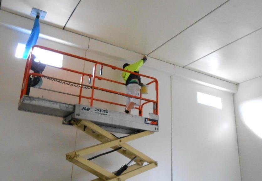 Person in high-visibility vest on a lift, working on a white ceiling.