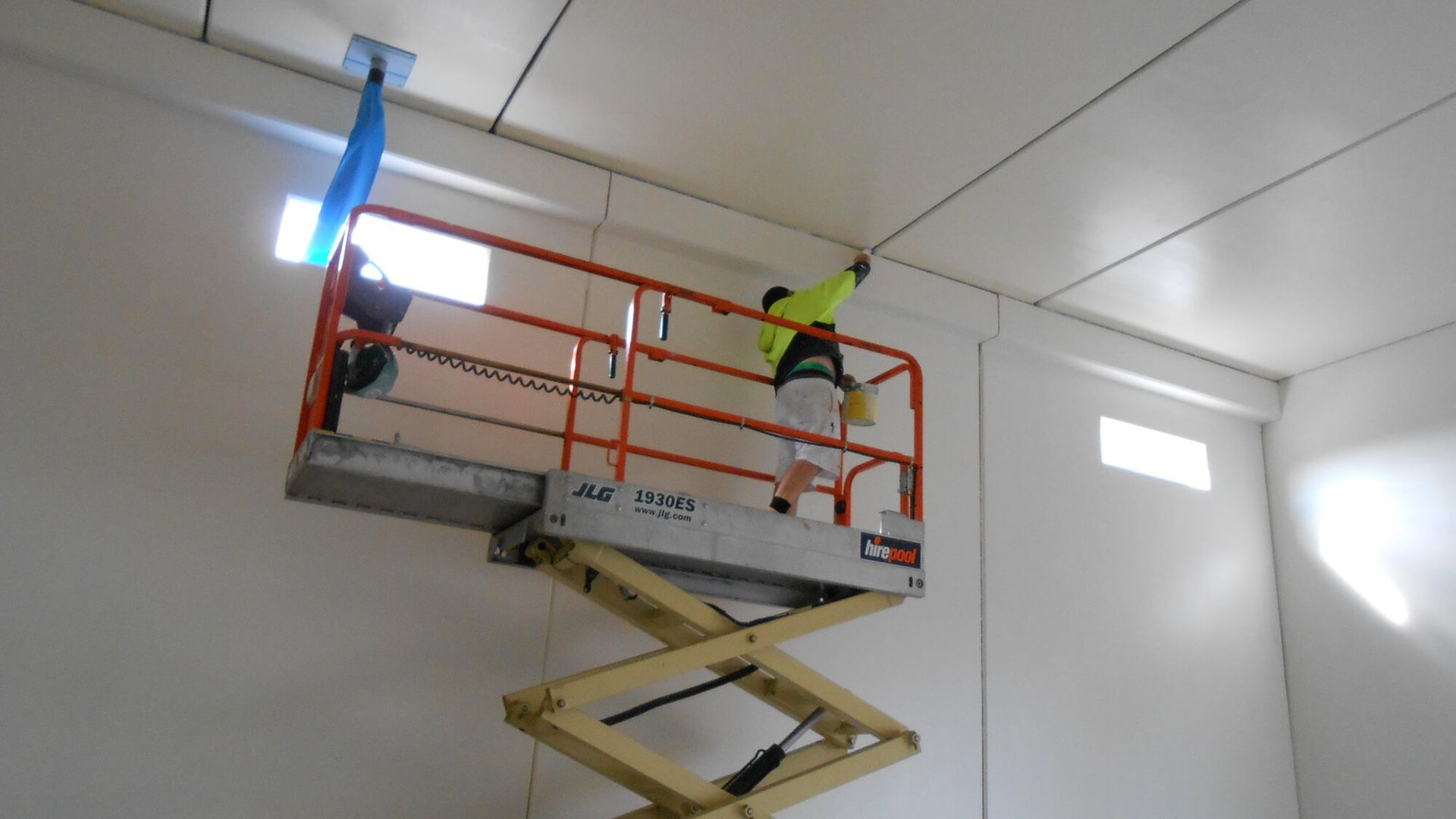 Construction worker on a scissor lift installing ceiling panels, indoors.