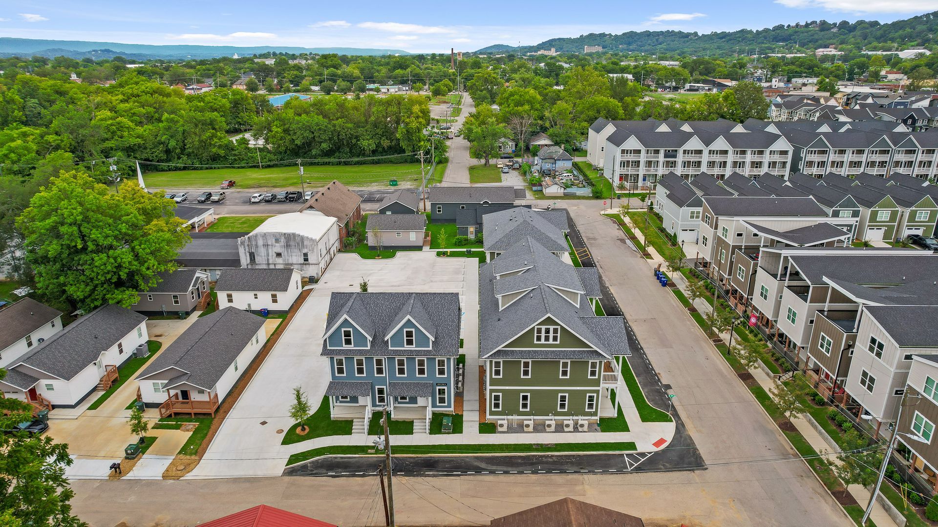 Aerial view of houses along a street with green trees and buildings. Cloudy sky.