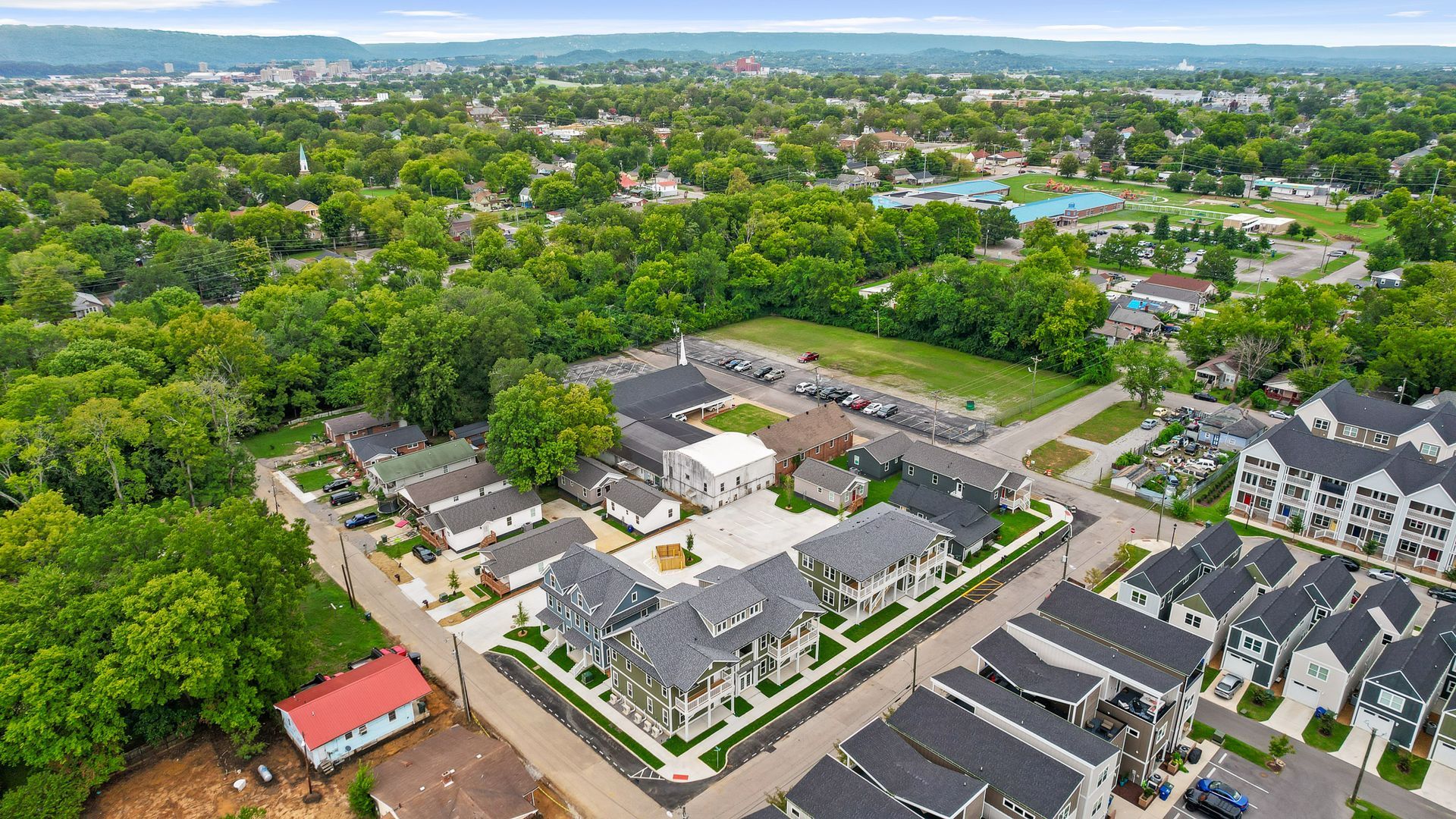 Aerial view of a neighborhood with houses, trees, and buildings; a town in the distance.