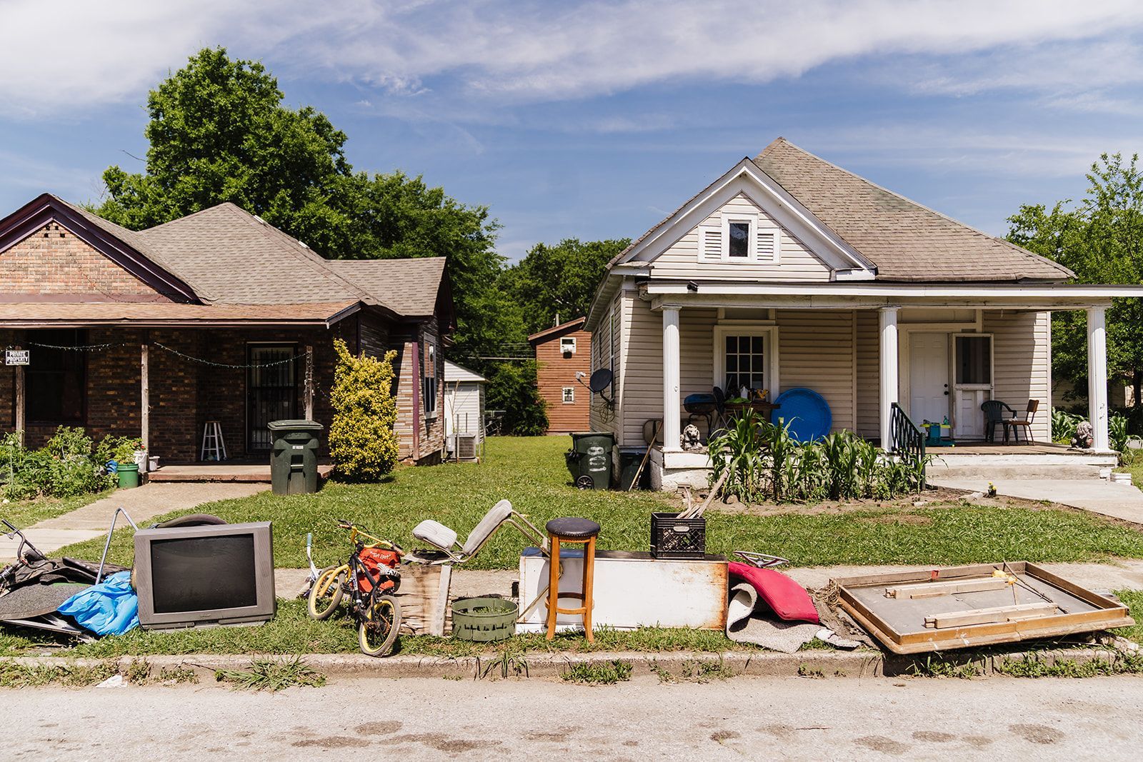 Houses with trash and debris along the curb. Brown and beige homes with a blue sky background, suggesting a neighborhood cleanup or moving process.