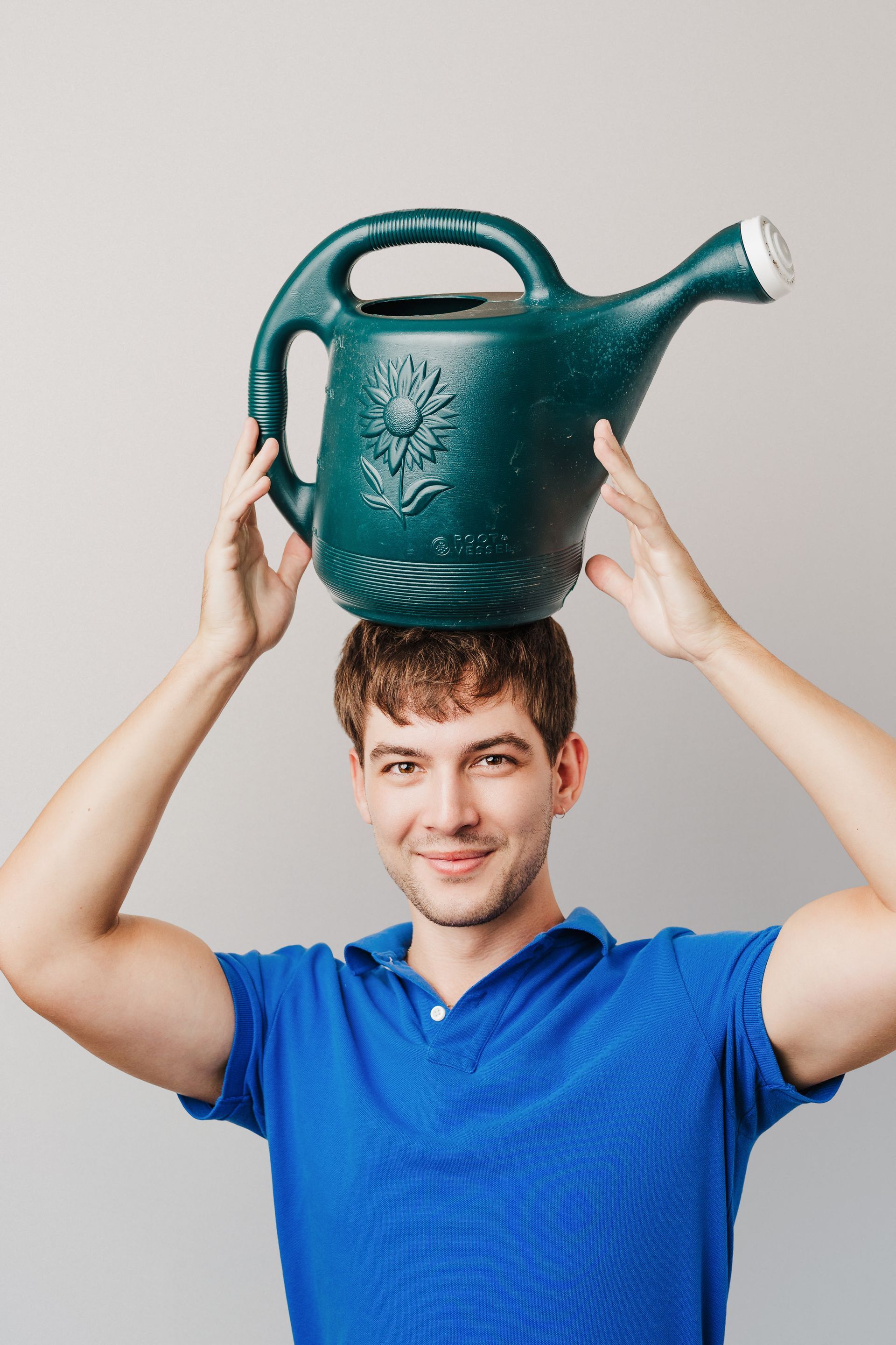 Teenager wearing a yellow apron, holding a red whisk and looking at a cookbook with a smile. Gray background.