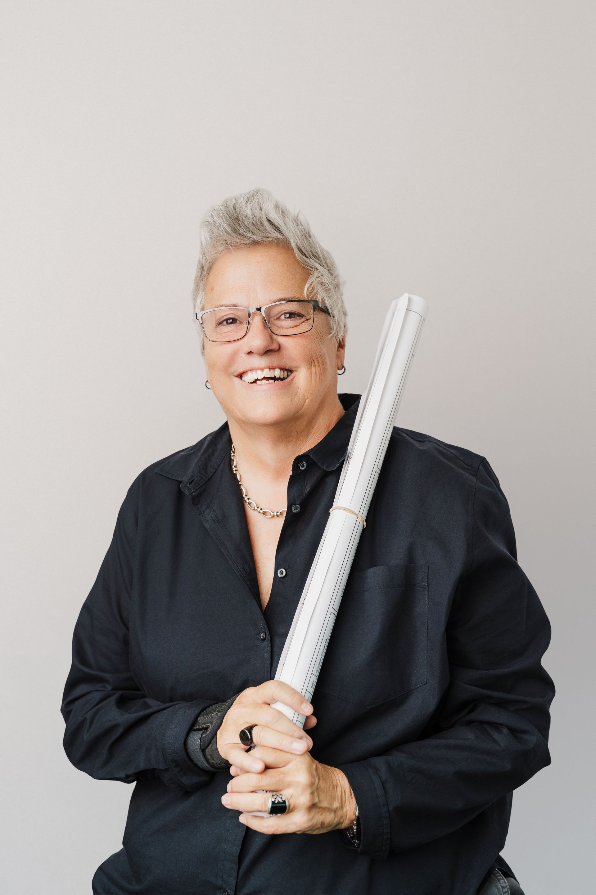 Person smiling, holding rolled-up papers, wearing glasses and a black shirt.