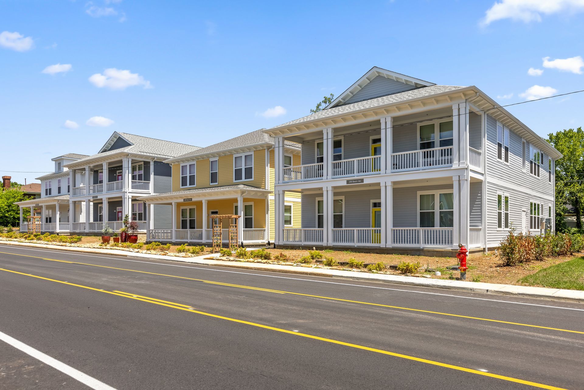 Two-story apartment buildings with white and yellow exteriors, each with a covered porch, sit along bailey avenue.