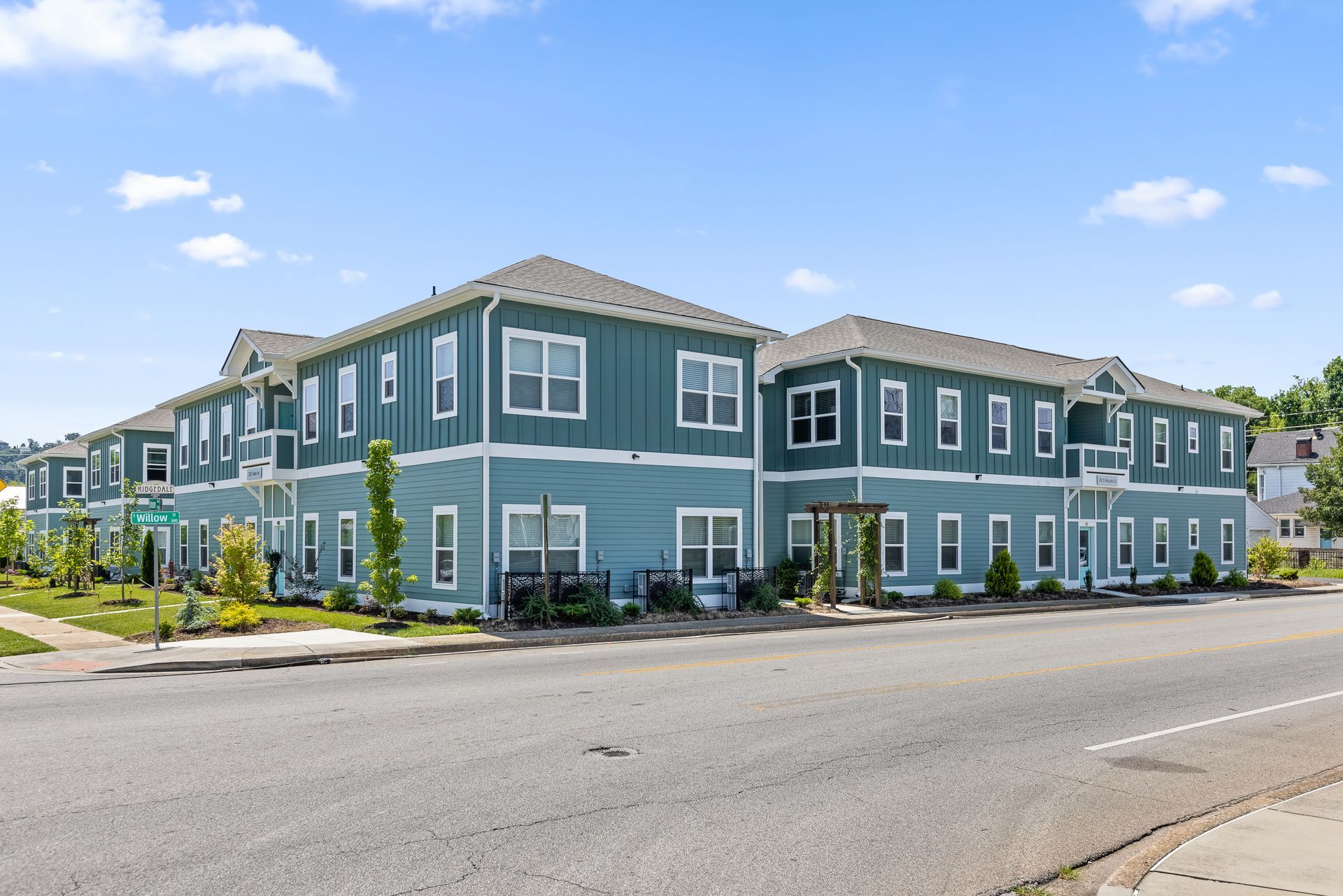 Two-story teal apartment building with white trim, viewed from across a street on a sunny day.