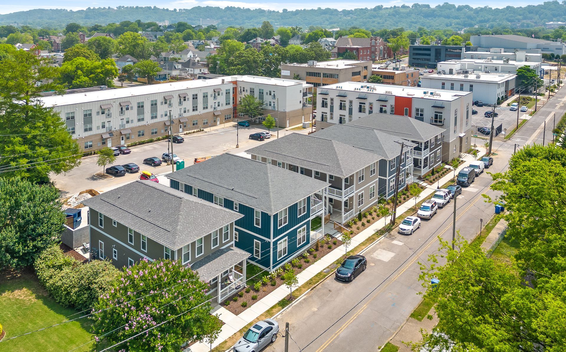 Aerial view of multi-unit residential buildings along a street, with parked cars and trees.