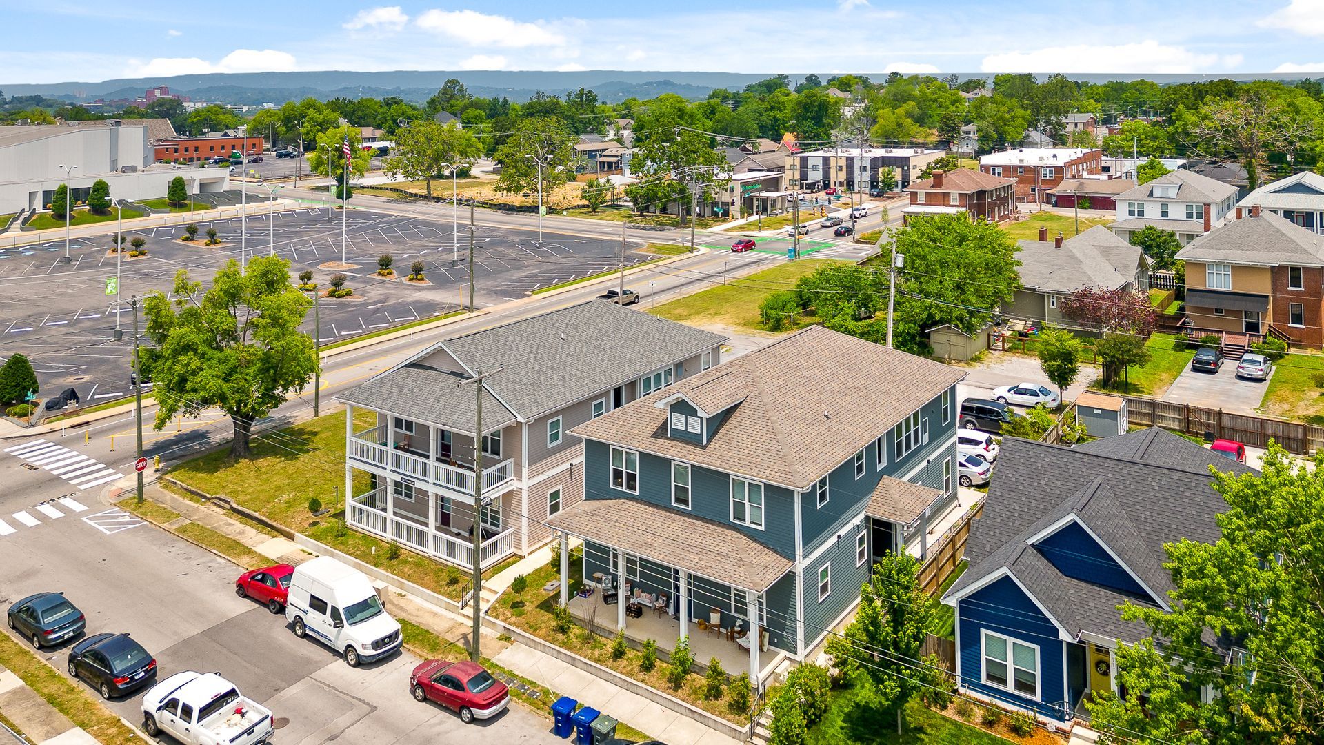 Aerial view of houses along a street, some with porches. A parking lot is in the distance.