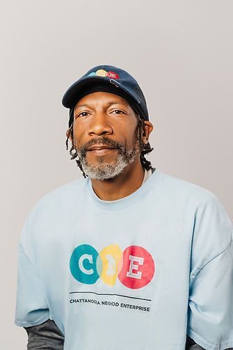 Man with dreadlocks wearing a blue cap and light blue sweatshirt with the letters 