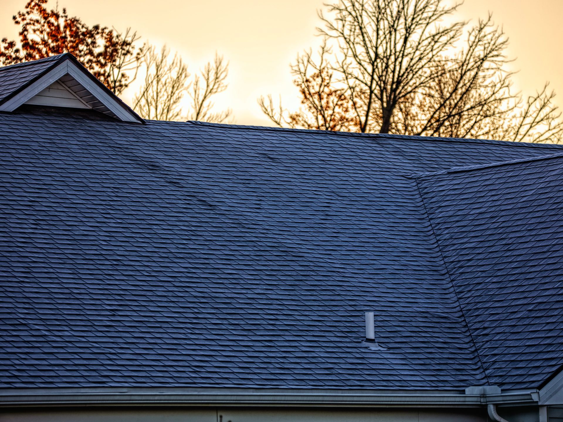 A roof of a house with a sunset in the background.