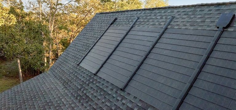 A roof with solar panels on it and trees in the background.