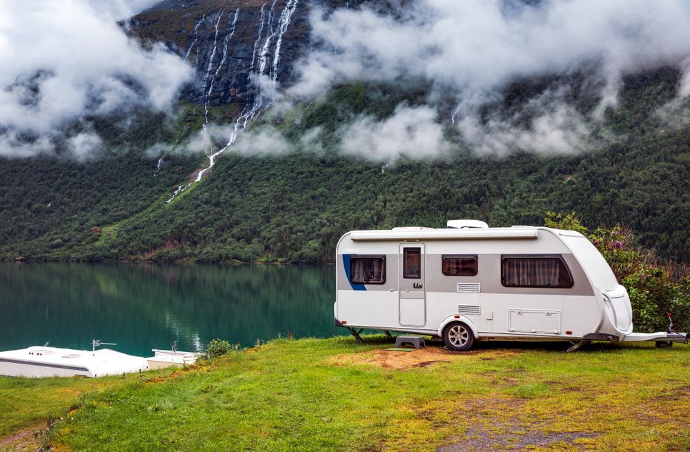 A white camper parked on a grassy bank overlooking a lake and mountains. — The Caravan Clinic in South Murwillumbah, NSW