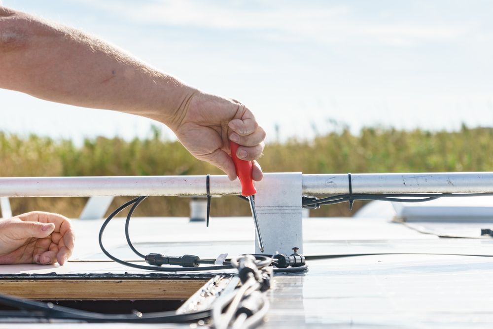 A person's hand uses a red screwdriver to tighten something on a white vehicle roof with a blue sky background. — The Caravan Clinic in South Murwillumbah, NSW