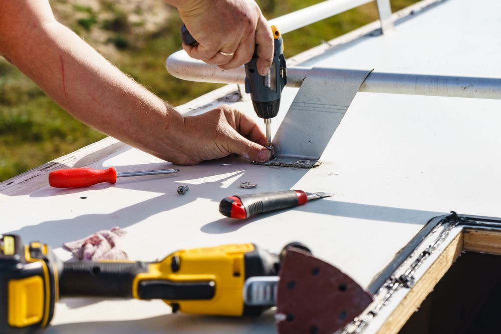 Person using a power drill to attach a metal hinge to a white surface outdoors. — The Caravan Clinic in South Murwillumbah, NSW