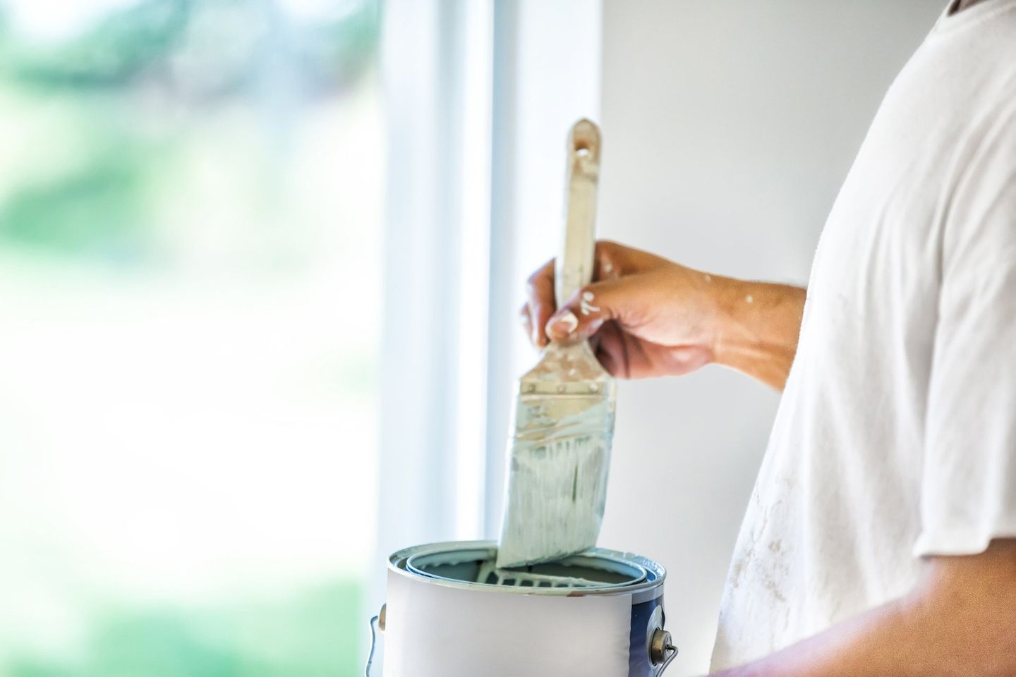 A house painter dips his brush into a can of paint