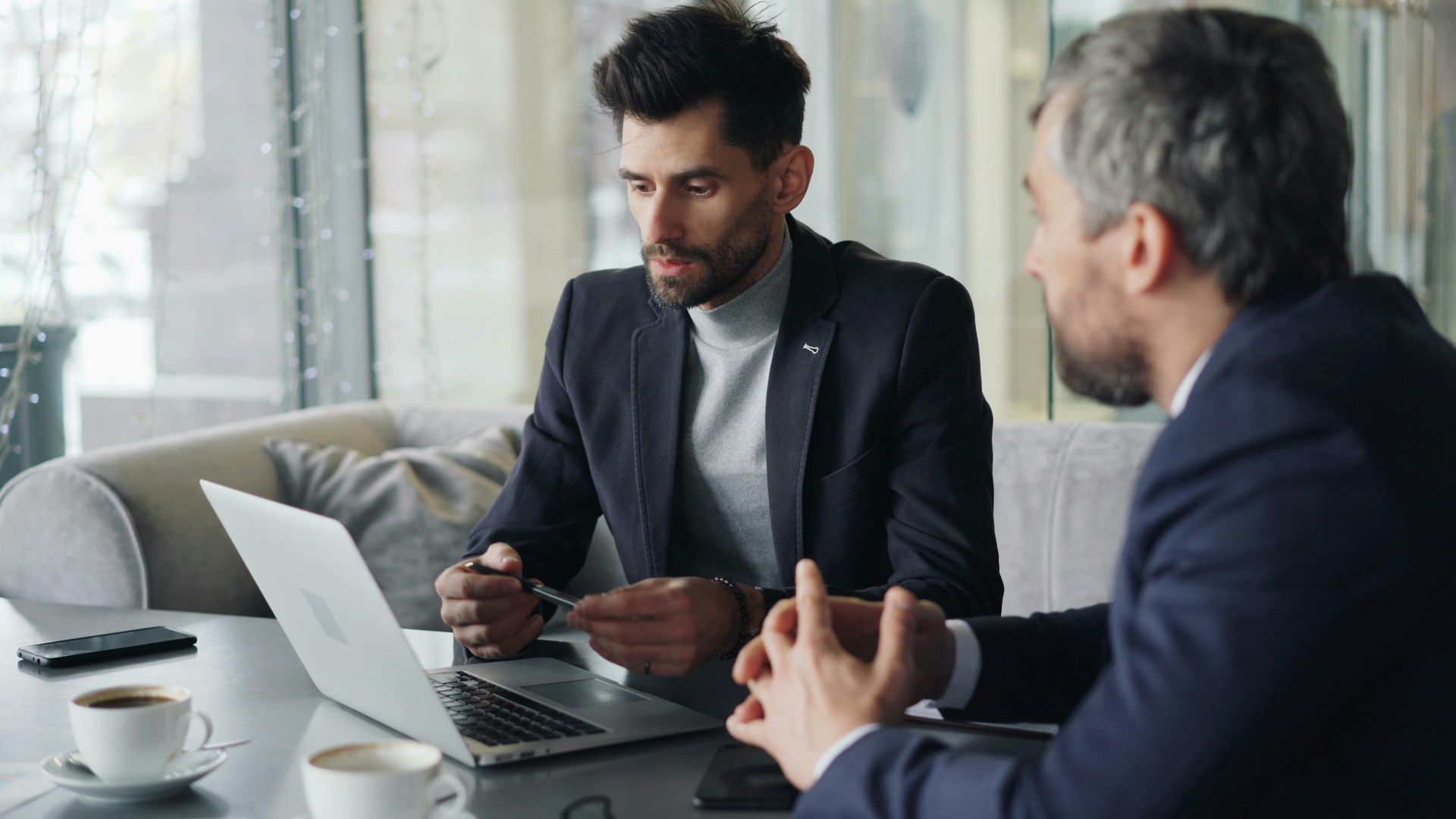 Two men are sitting at a table looking at a laptop.