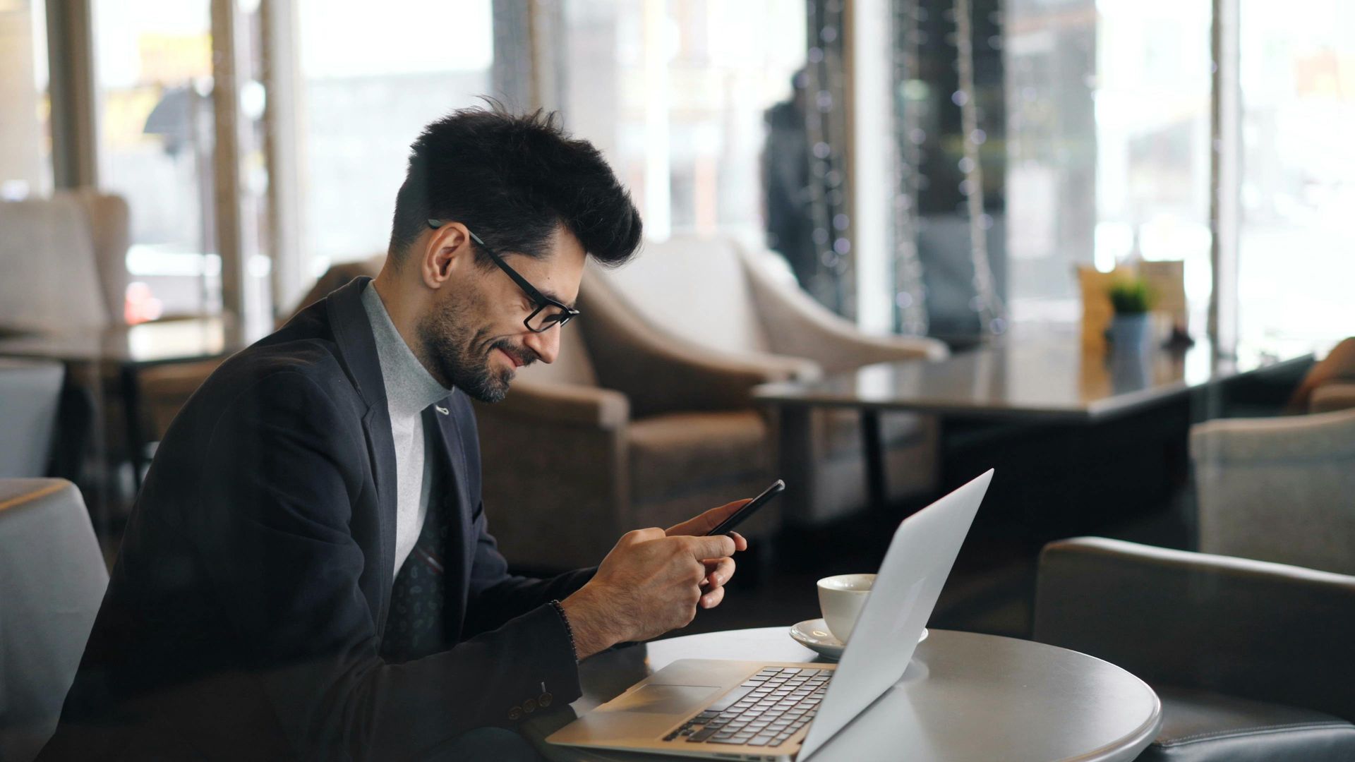 A man is sitting at a table with a laptop and a cell phone.