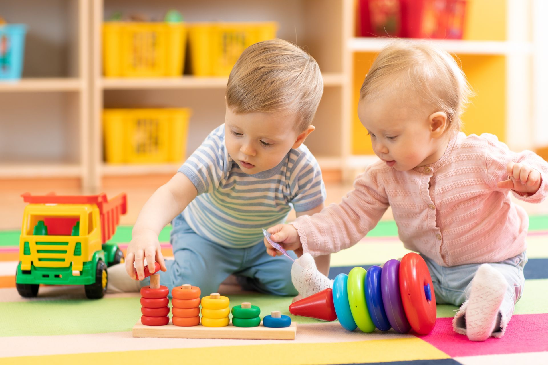 Preschool boy and girl playing on floor with educational toys.