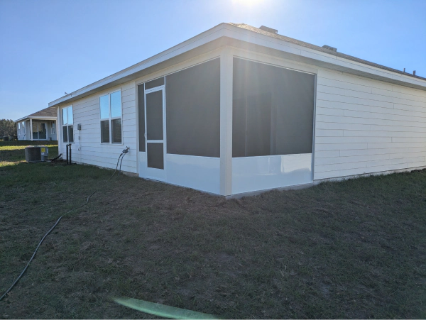 Exterior view of a white house with a screened-in porch. Bright sunlight illuminates the siding and grass.