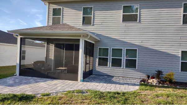 A screened-in porch with a brick patio is attached to a two-story gray house.
