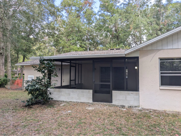 Back exterior of a beige house with a screened-in porch and surrounding trees in a natural setting.
