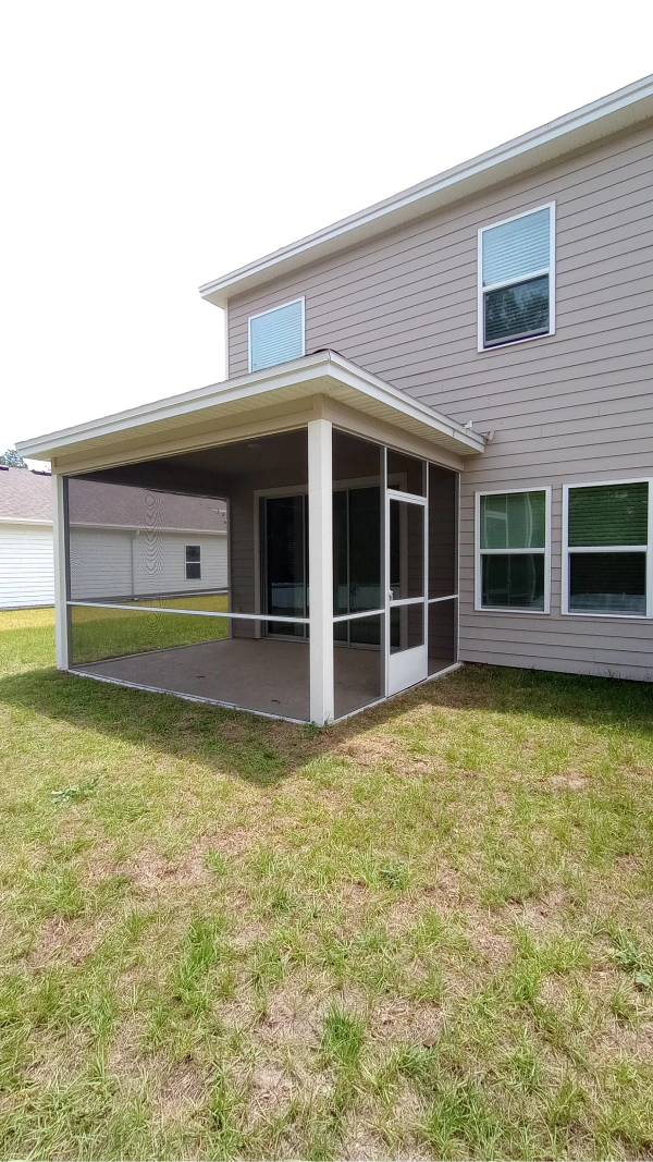 Screened patio attached to a two-story house with tan siding, surrounded by green grass.