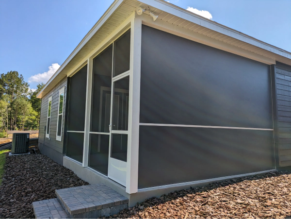 A screened porch with black sun shades on a sunny day. Grey siding and white trim are visible.