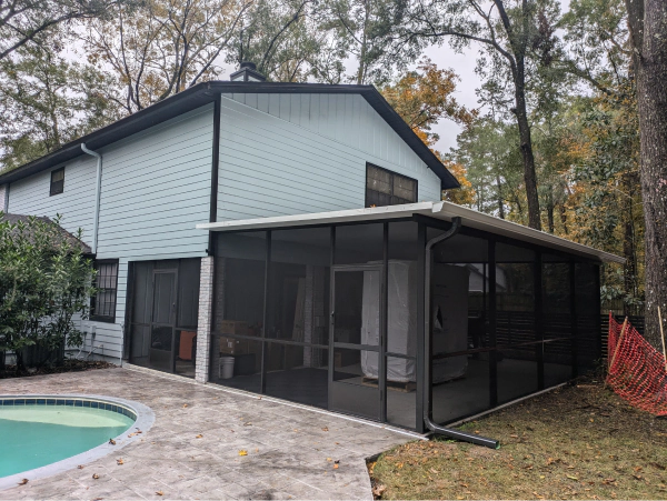 A two-story house with a screened porch next to a pool. The house is light blue with a dark roof and black screen frames.