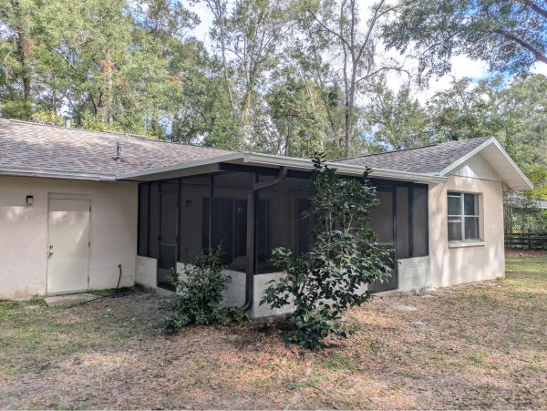 Exterior view of a single-story home with a screened porch, beige siding, and a gray roof, set in a grassy backyard.