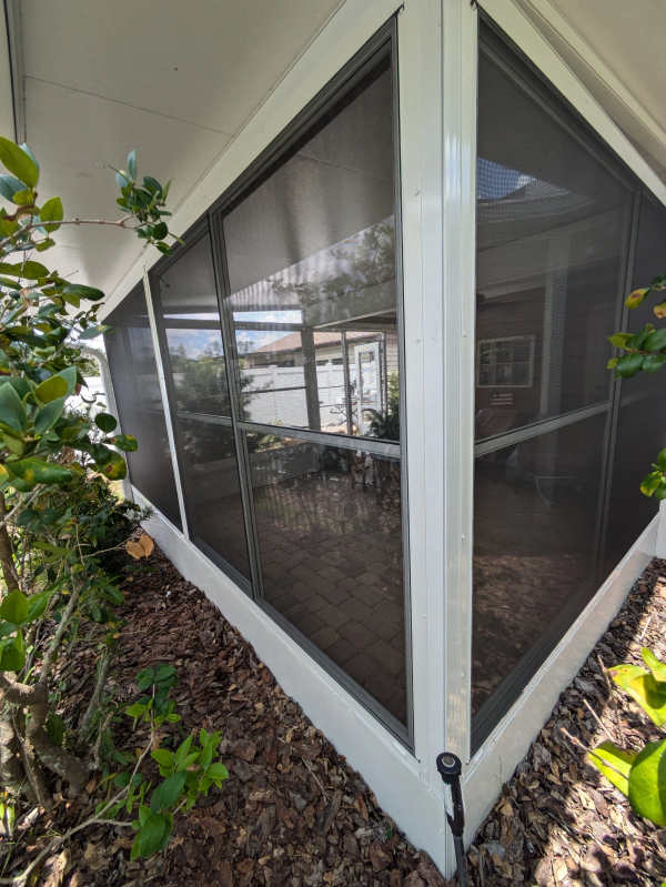Corner view of a screened porch with white frames, dark screens, and a water view visible through the screens.