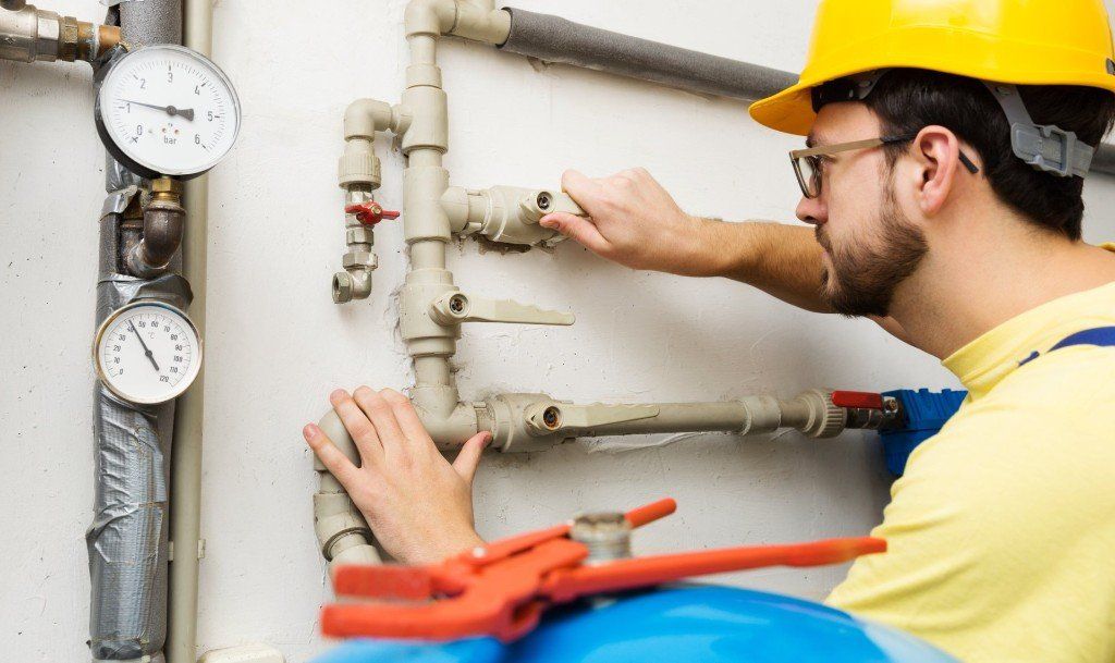 A man wearing a hard hat is working on a water pipe.