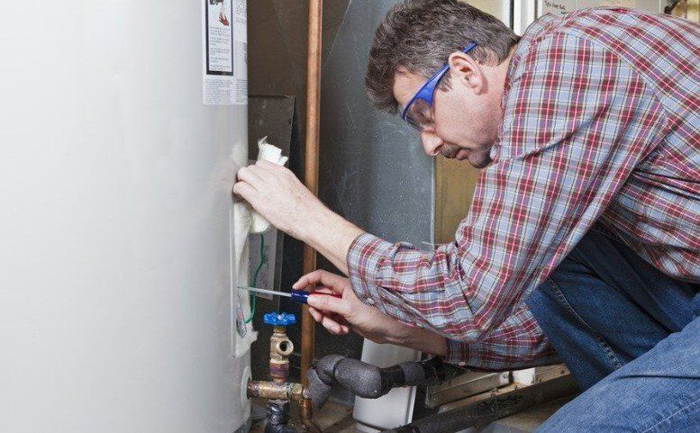 A man is working on a water heater with a screwdriver.