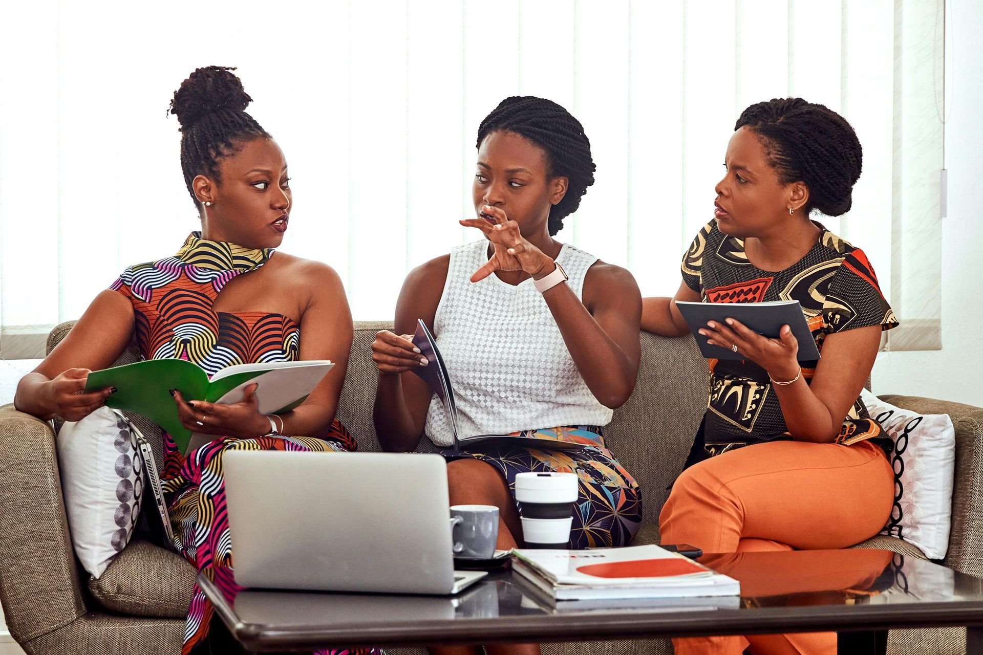 Three women are sitting on a couch with a laptop and a tablet.