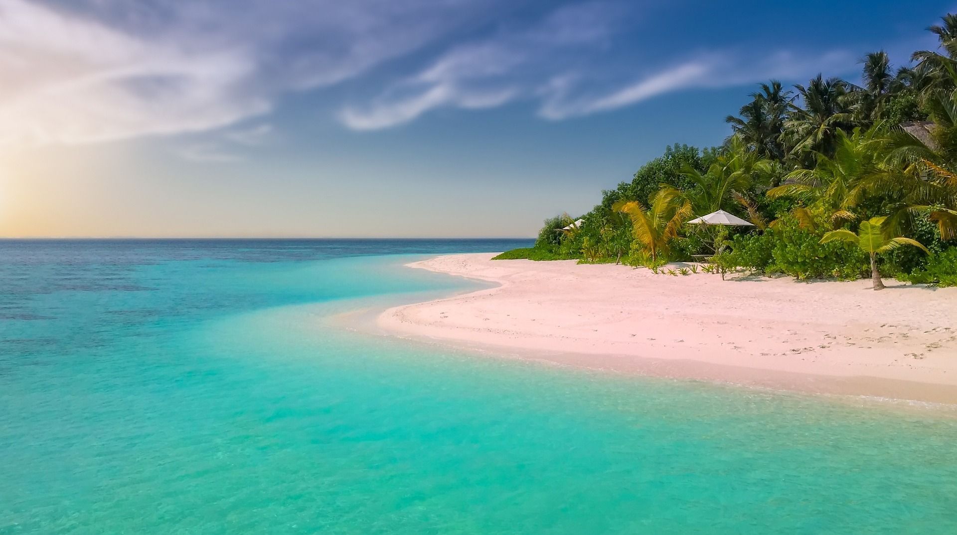 A tropical beach with clear, blue water, white sand, and lush, green vegetation.