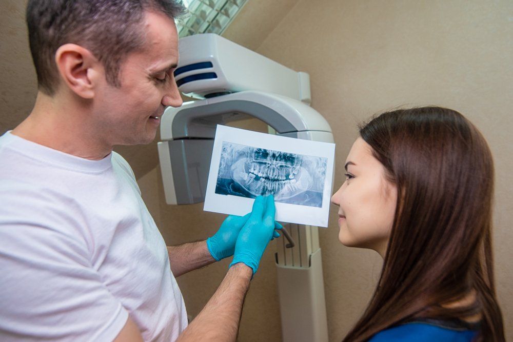 A dentist is looking at an x-ray of a woman 's teeth.
