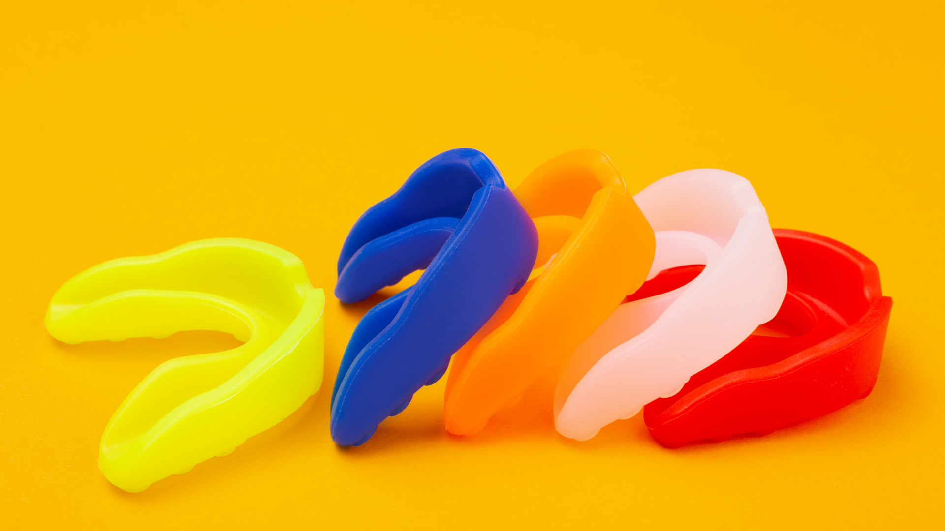 A group of colorful mouth guards are sitting on top of each other on a yellow surface.