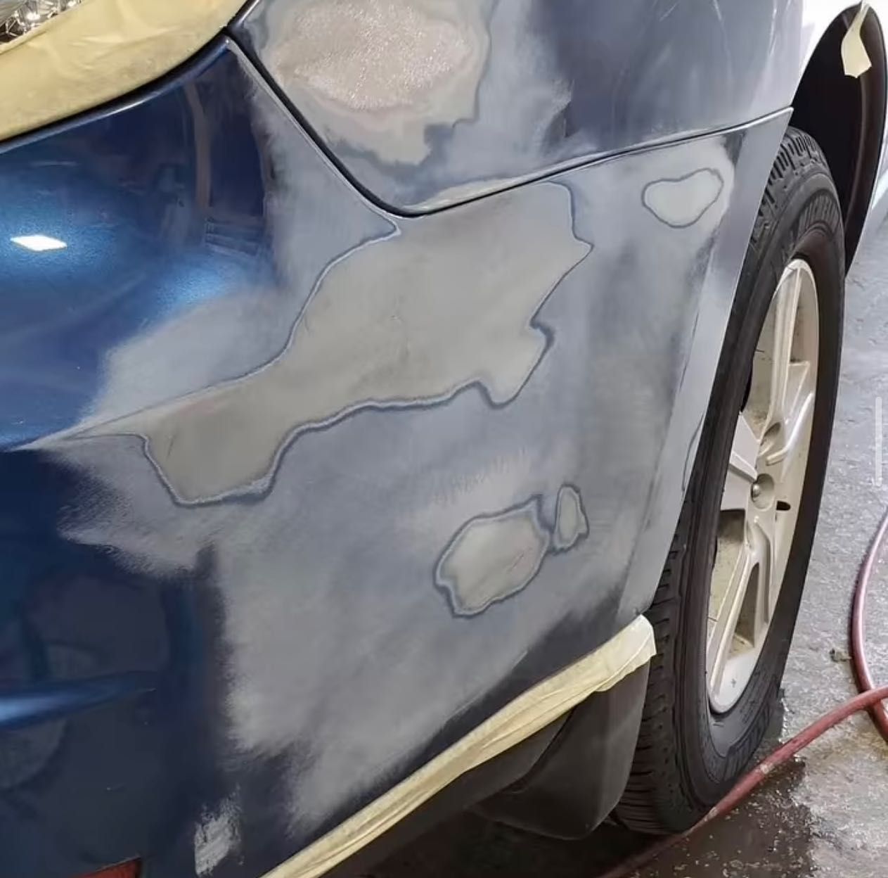 A blue car is being painted with a hose attached to it.