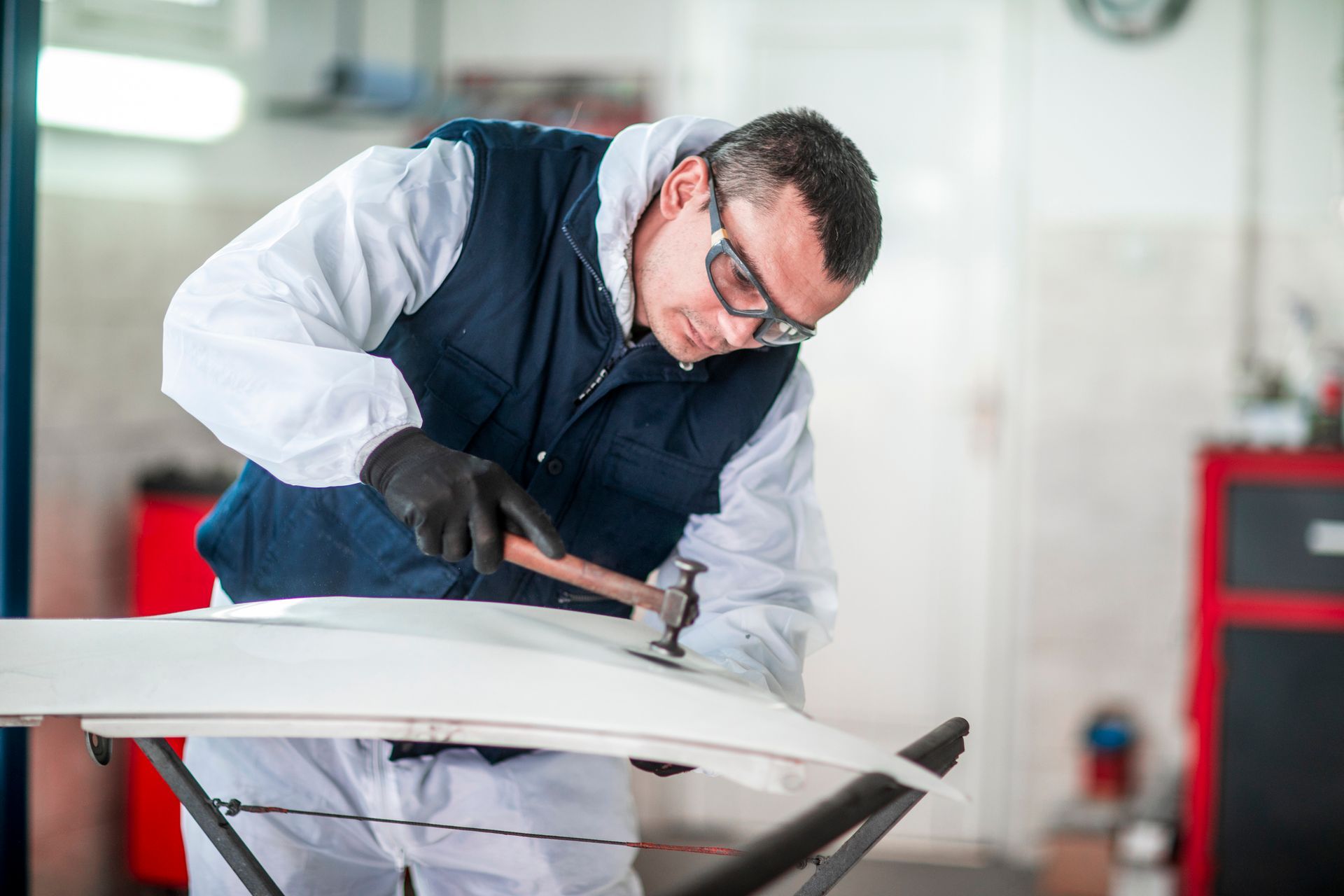 A man is working on a car hood with a hammer.